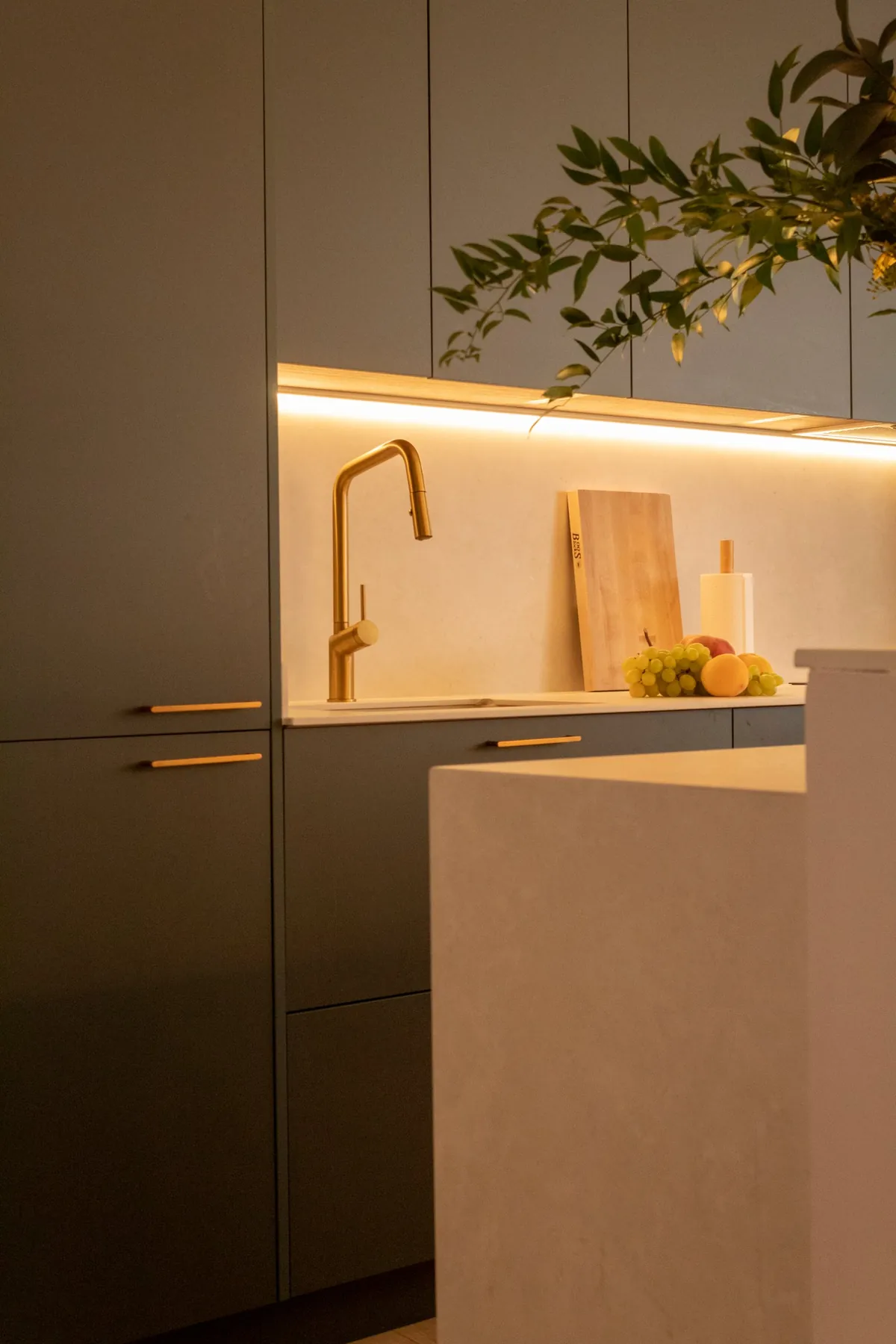 Cocina en verde con tiradores y grifo dorados y frente iluminado